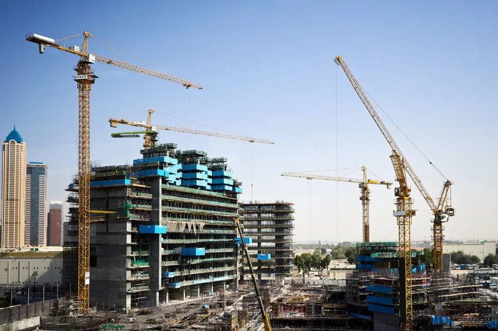 High-rise buildings under construction wrapped in scaffolding, with several tower cranes against a clear sky